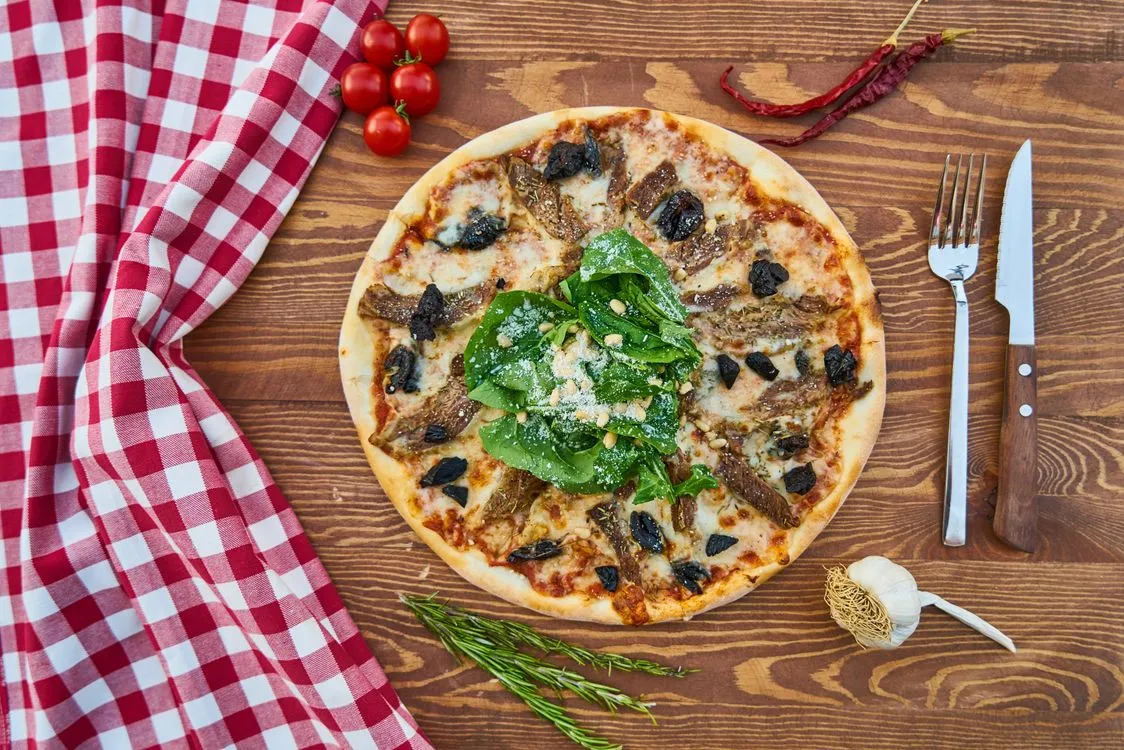 Pizza surrounded by fresh ingredients on a wooden table