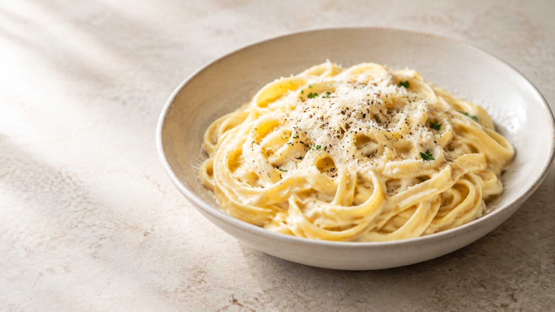 A bowl of glossy classic fettuccine Alfredo with Parmesan and cracked black pepper