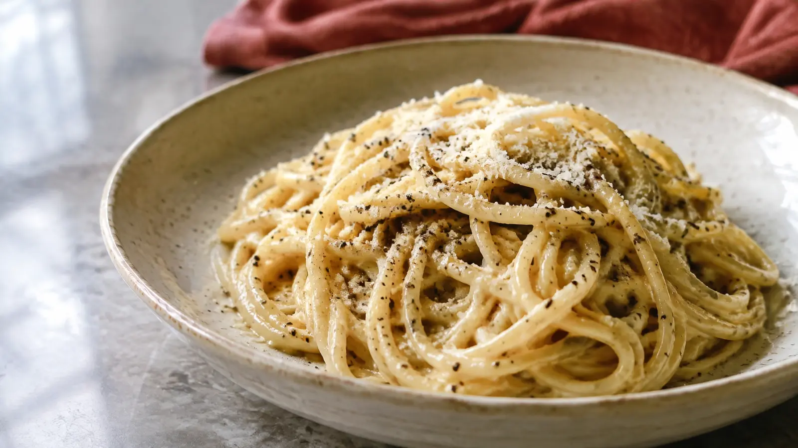 Finished cacio e pepe spaghetti served in a cream ceramic bowl